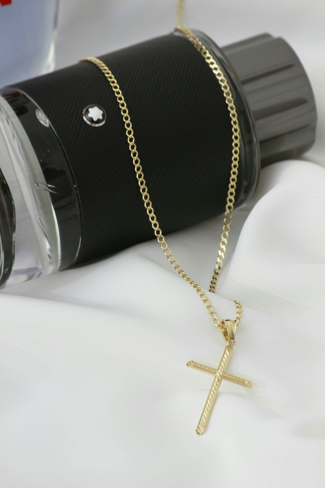 A cross pendant on a chain next to a cup