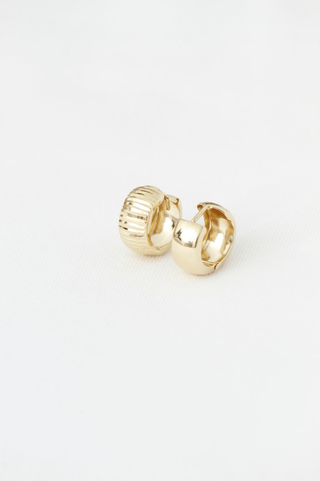Two textured and smooth gold hoop earrings on white.