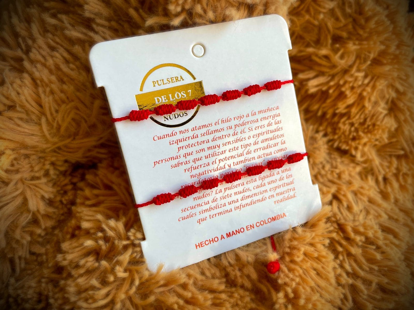Dos pulseras de 7 nudos en hilo rojo sobre un cartón con la historia inspiradora de su significado, representando un lazo de amor y protección inseparable para parejas